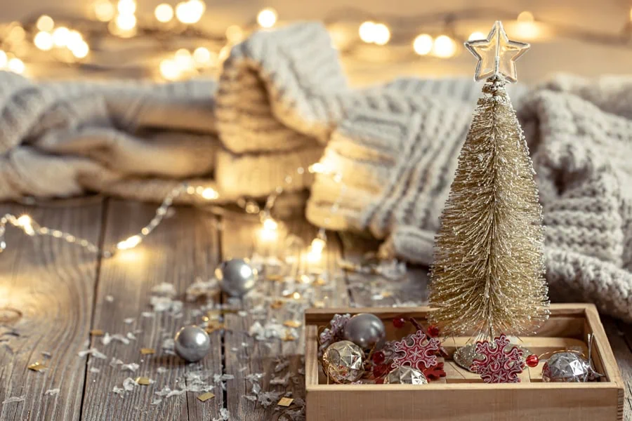 Kleine Weihnachtsbaum-Deko mit Lichterkette, Christbaumschmuck und gestrickter Decke im Hintergrund.