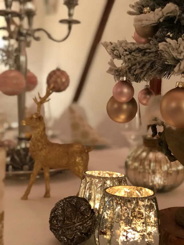 Weihnachtsdeko mit goldener Hirschfigur, Kerzenhaltern und Christbaumkugeln in sanften Rosé- und Goldtönen.